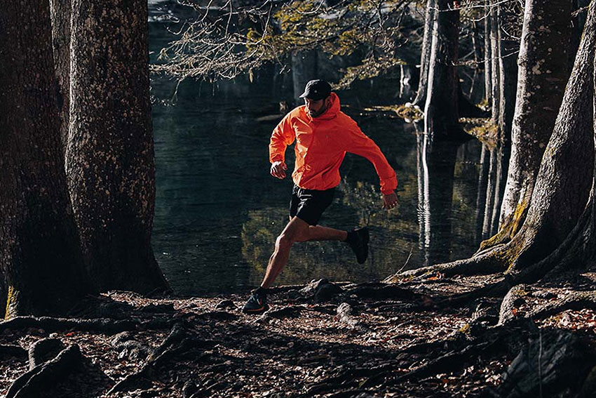 Man running in forest wearing orange Mac in a Sac jacket